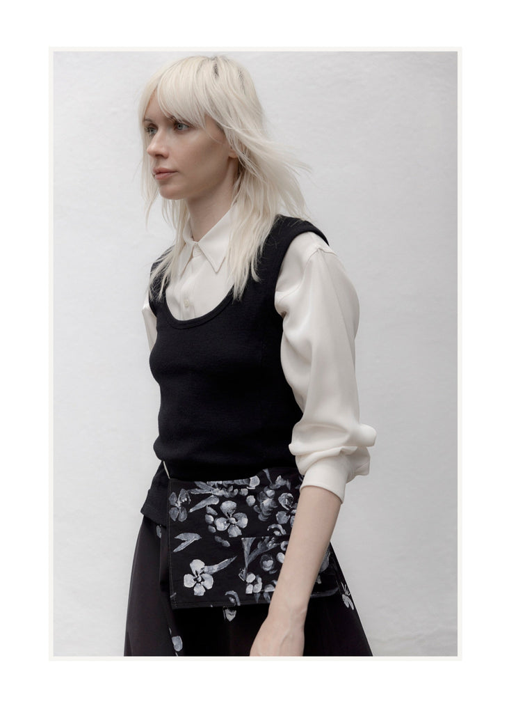 Person wearing a black sleeveless top and floral skirt against a white background