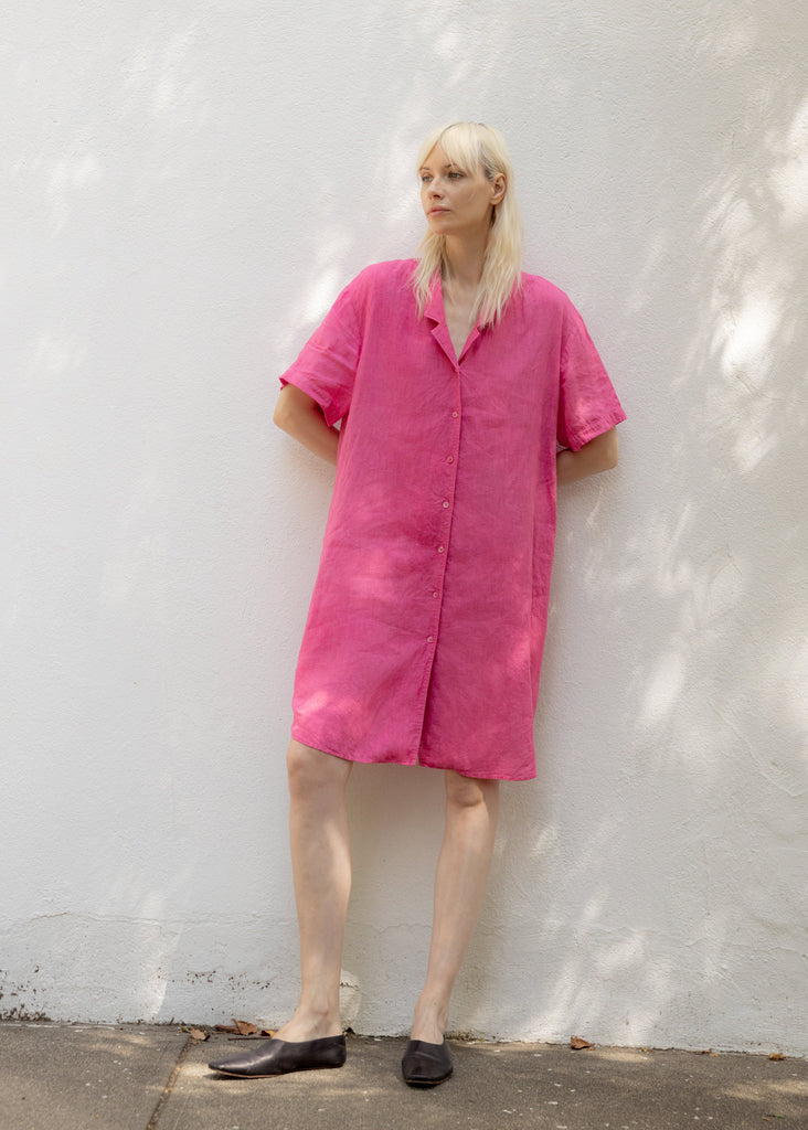Person wearing a bright pink dress standing against a white wall.