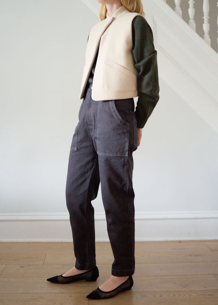 Person wearing a cashmere vest over a dark green sweater and dark pants in a minimal indoor setting.
