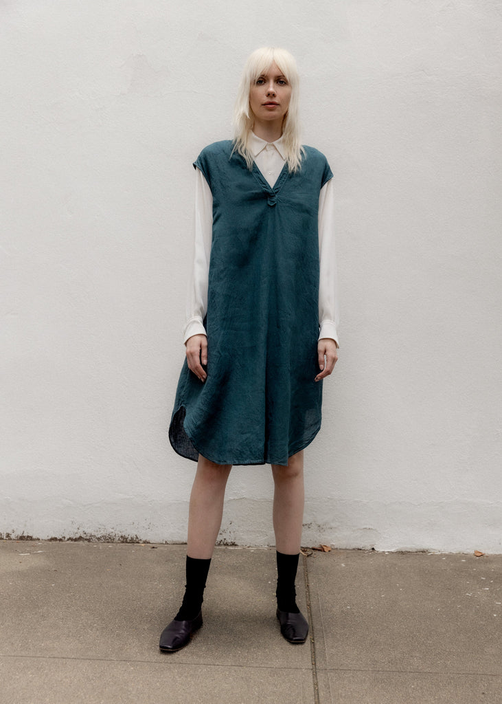 Person wearing a teal dress over a white shirt against a plain wall.