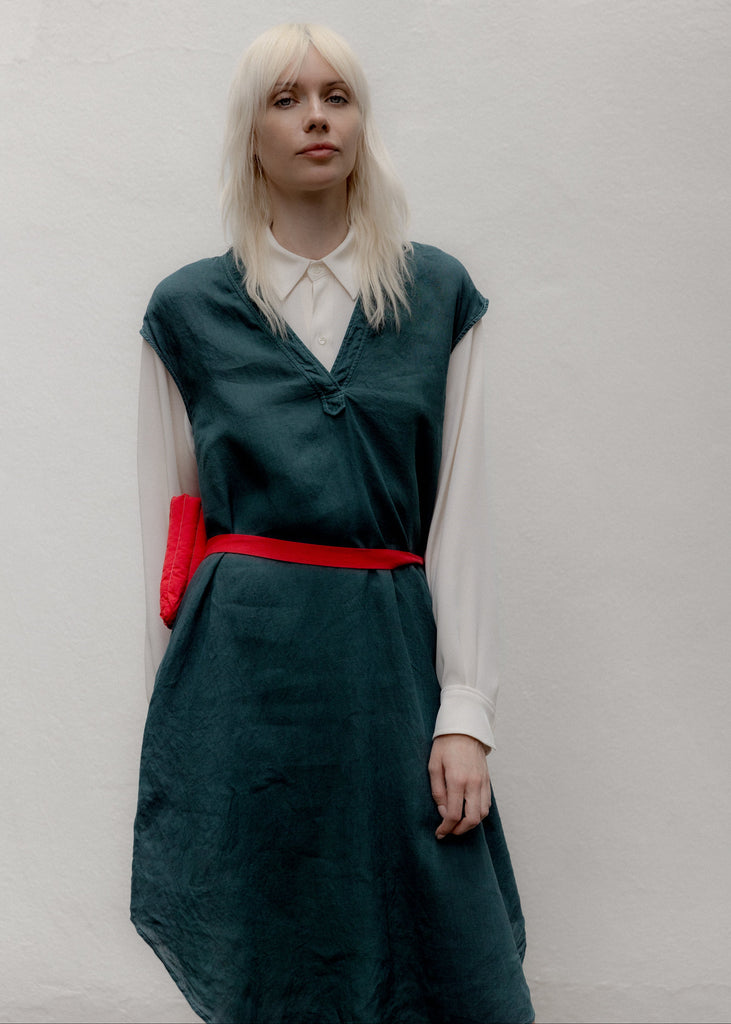 Person wearing a green dress with a red belt against a plain background