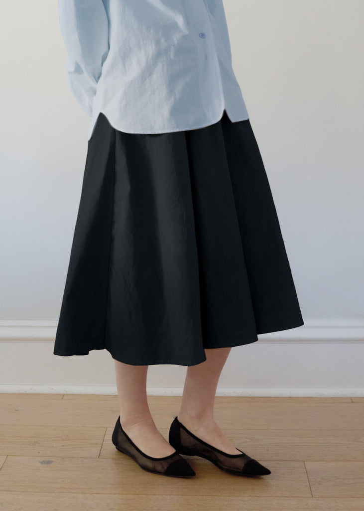 Person wearing a light blue shirt, black skirt, and black shoes on a plain background