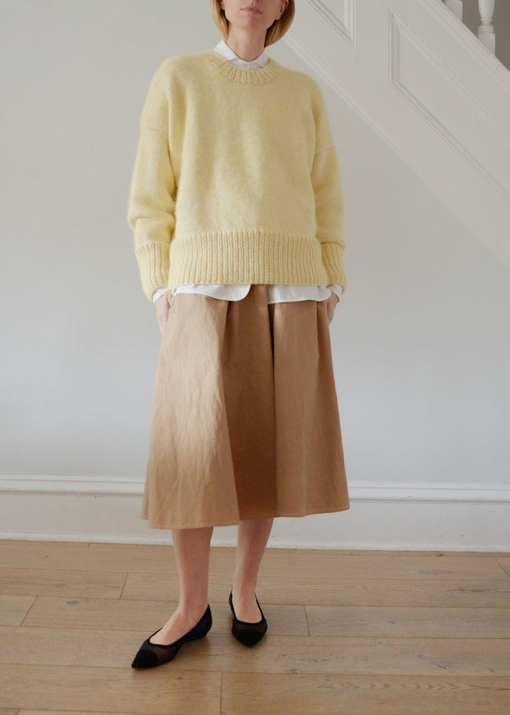 Person wearing a yellow sweater and brown skirt standing on a wooden floor.