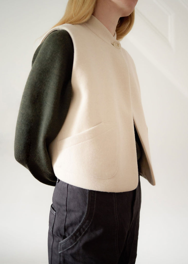 Person wearing a beige cashmere vest over a green sweater with a plain background