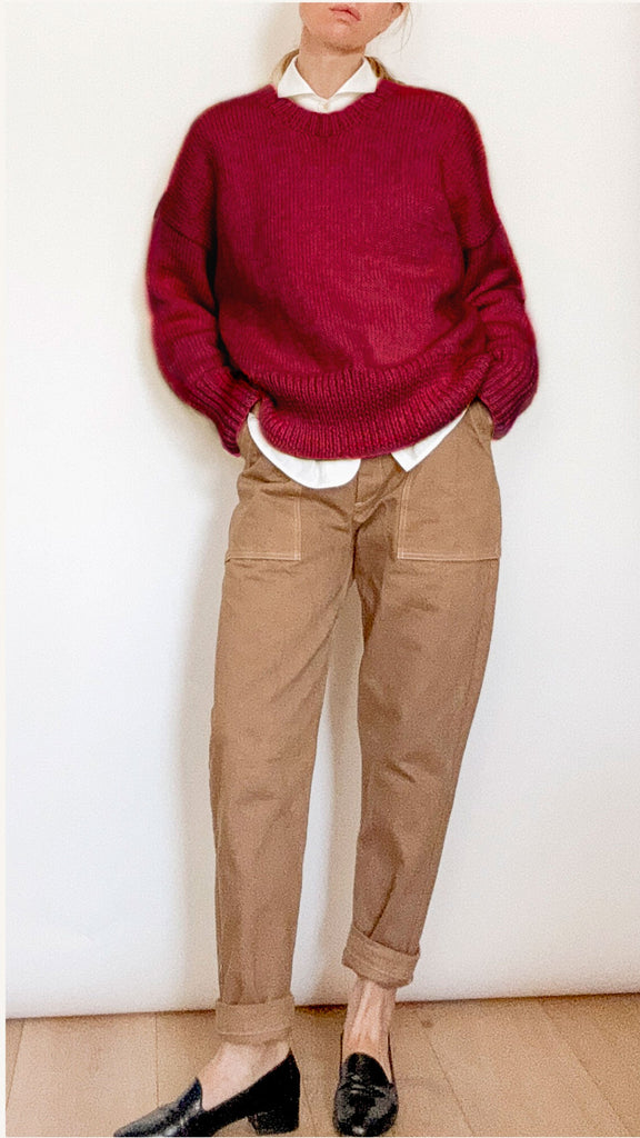 Person wearing a red sweater, white shirt, beige pants, and black shoes against a white background