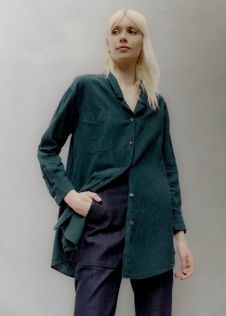 Person wearing a dark green shirt and navy pants against a plain background