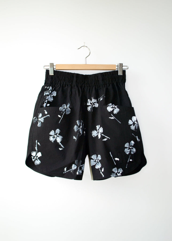 Black shorts with white floral pattern on a hanger against a white background