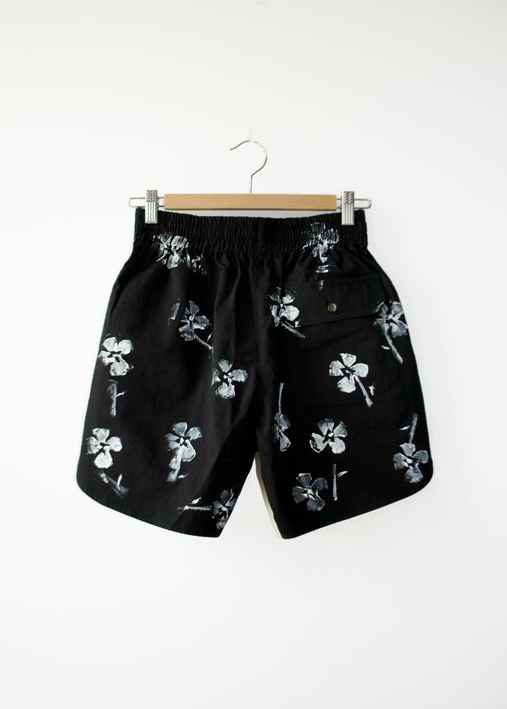 Black shorts with white floral patterns on a hanger against a white background