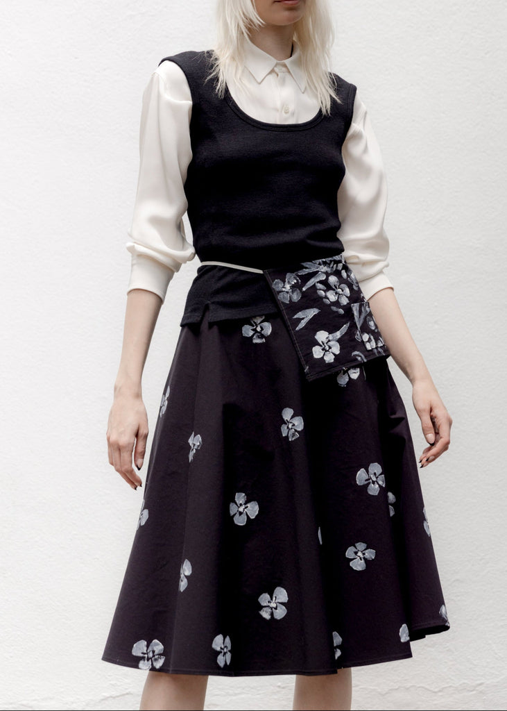 Person wearing a black sleeveless top and floral skirt with a white shirt underneath on a white background