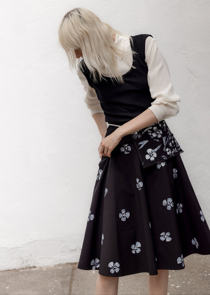 Person wearing a black dress with floral patterns against a white wall.