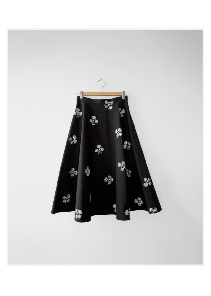 Black skirt with white floral pattern on a hanger against a white background