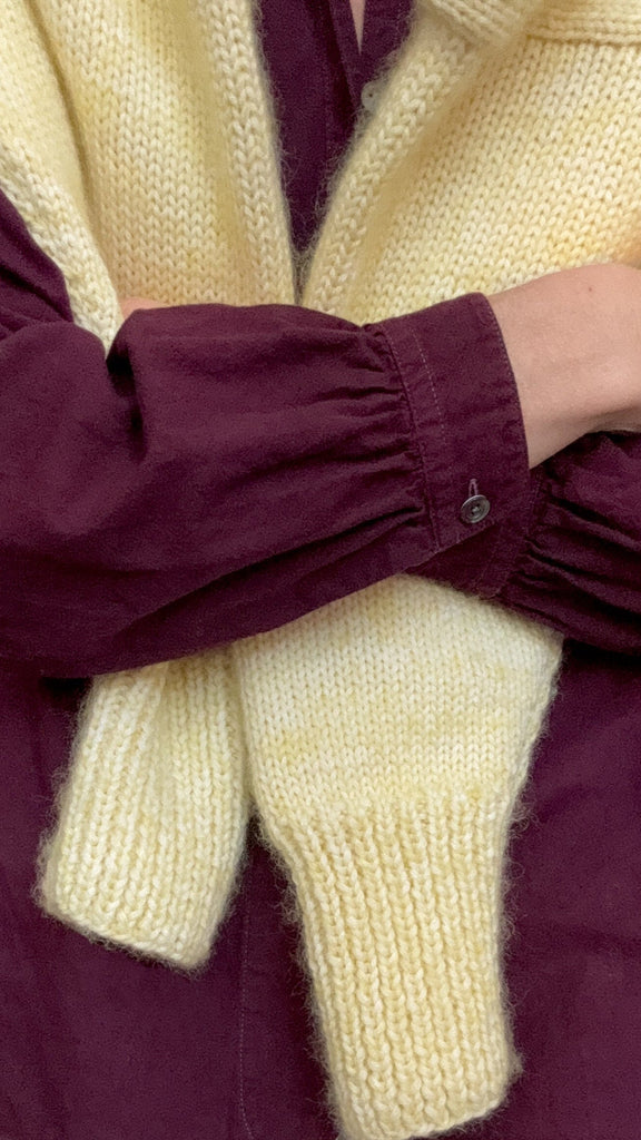 Close-up of a person wearing a burgundy shirt with a pale yellow sweater.