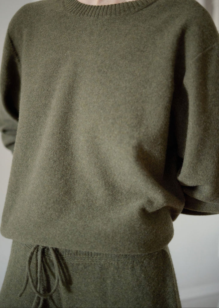 Person wearing a green sweater and pants against a plain background