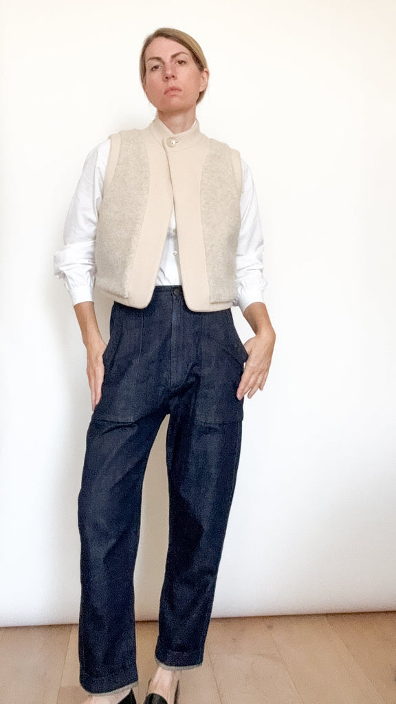 Person wearing a cream vest over a white shirt and dark blue pants on a plain background