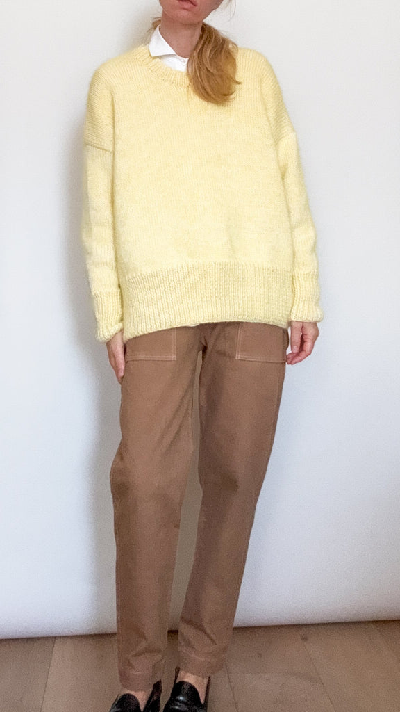 Person wearing a light yellow sweater, dark beige pants, and black shoes against a white background