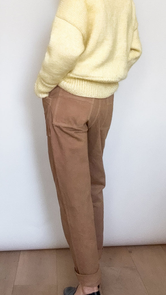Person wearing a light yellow sweater, dark beige pants, and black shoes against a white background